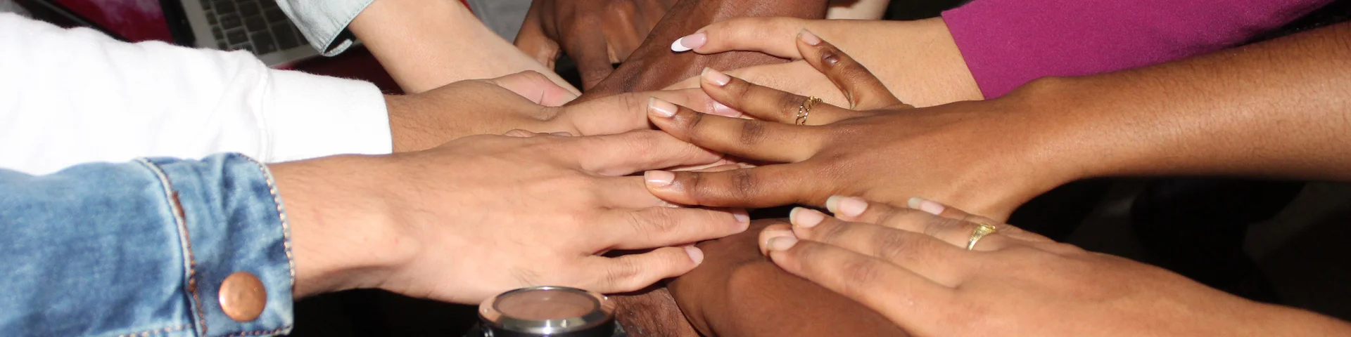 8 people's arms of different skin colors touching hands in a circle